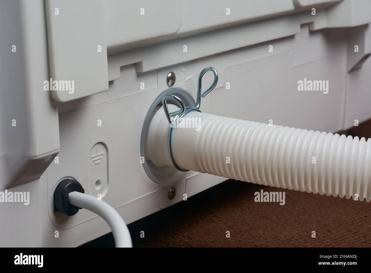 primo piano del tubo flessibile di scarico bianco collegato all'uscita del pannello posteriore della lavatrice con morsetto in metallo, messa a fuoco selettiva con spazio di copia Foto Stock