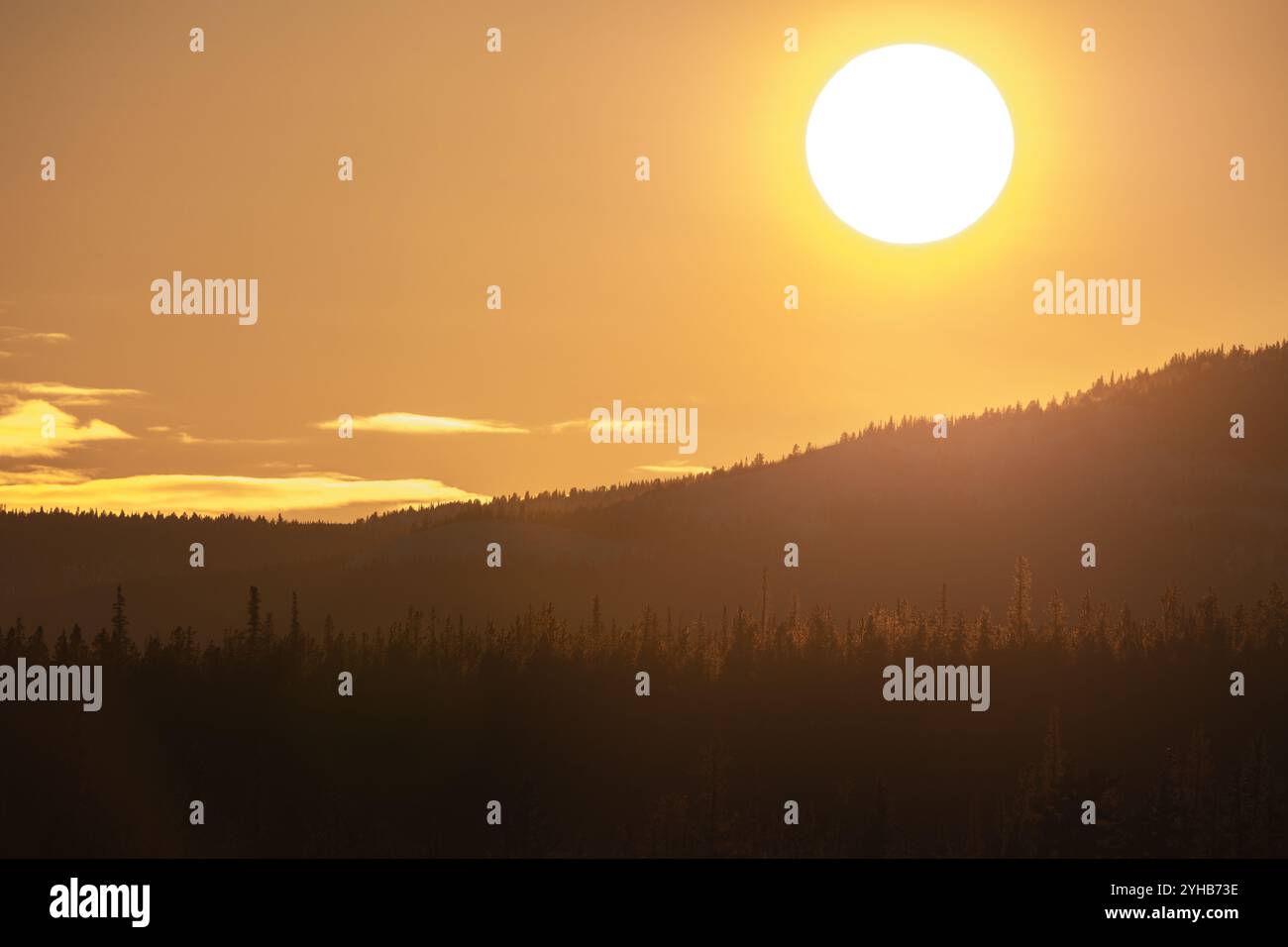 Il luminoso sole giallo arancione che tramonta sulla sagoma scura delle montagne del Canada settentrionale durante la primavera. Ottimo sfondo naturale. Foto Stock