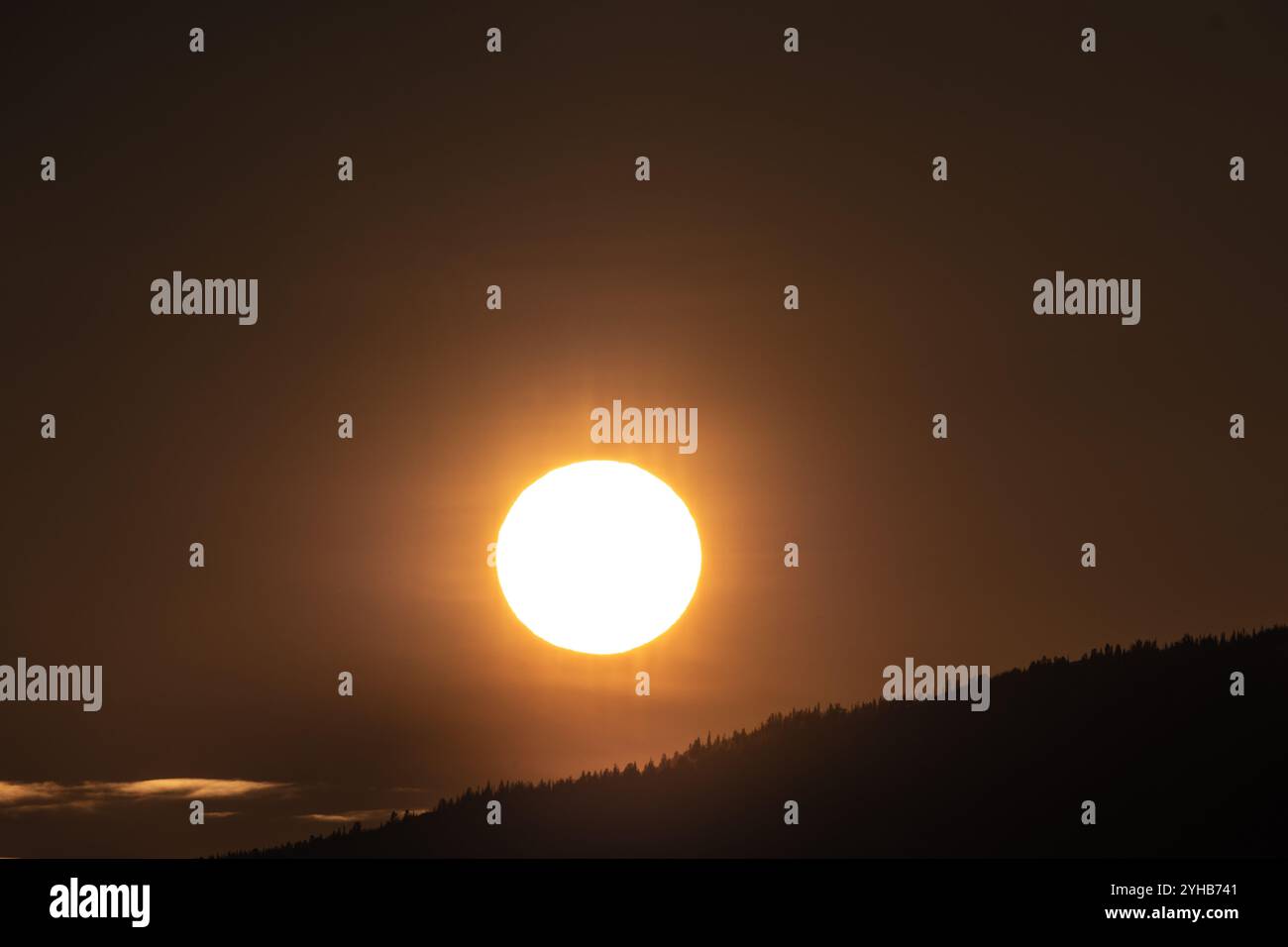 Il luminoso sole giallo arancione che tramonta sulla sagoma scura delle montagne del Canada settentrionale durante la primavera. Ottimo sfondo naturale. Foto Stock