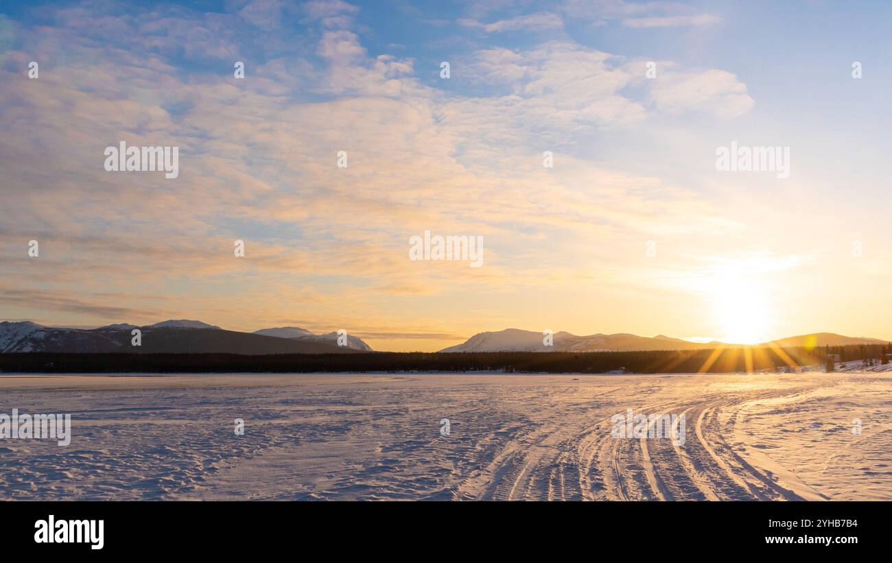 Tramonto su un lago ghiacciato nel nord del Canada durante la fine dell'inverno all'inizio della primavera. I raggi del sole brillano sulle cime delle montagne con nuvole. Foto Stock