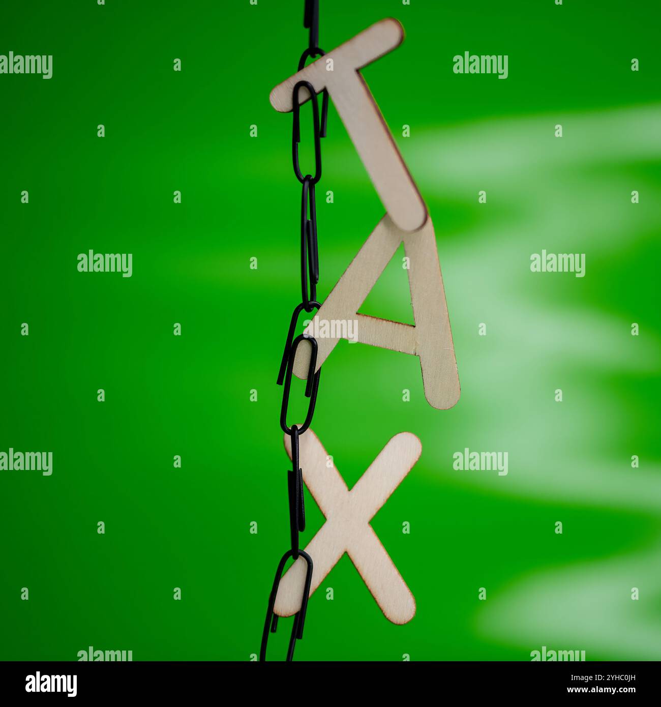 Lettere di legno che scrivono la parola "TASSA" appesa su graffette nere su sfondo verde Foto Stock