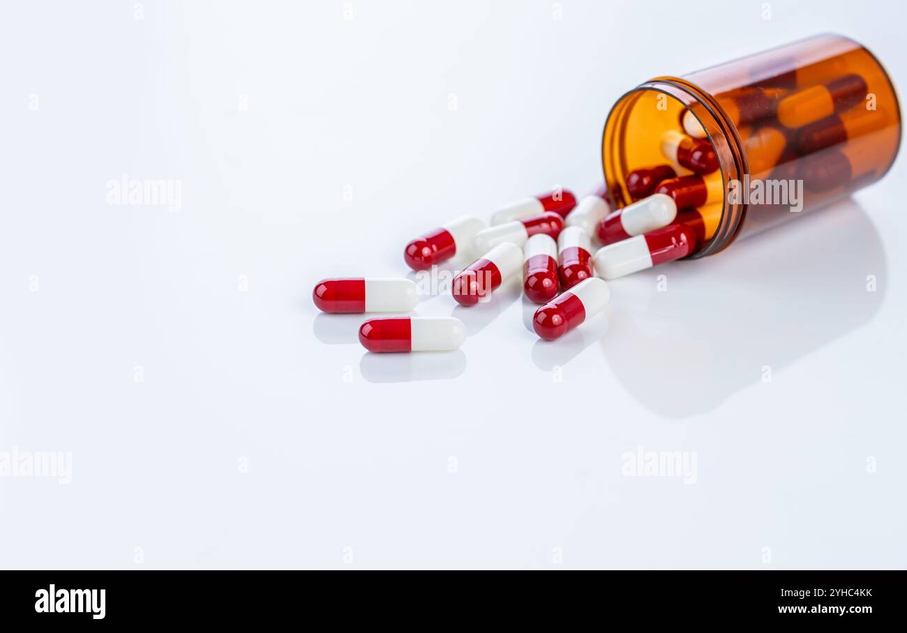 Capsule di prescrizione rosse e bianche che fuoriescono da un contenitore di plastica. Farmaci farmaceutici regolamentati. Enfatizzare gli standard di sicurezza, i farmaci Foto Stock