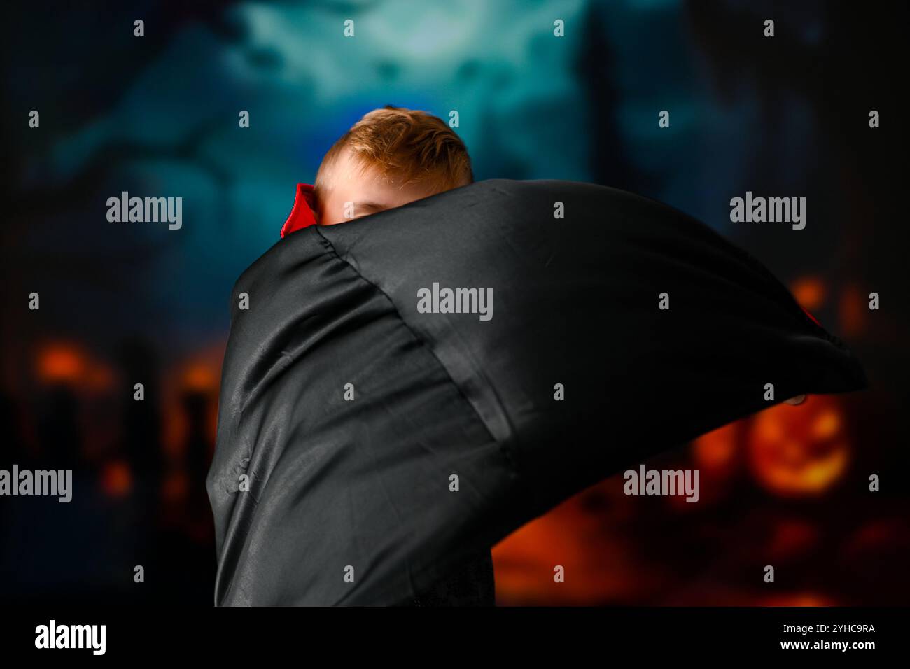 Bambino vestito da vampiro che posa di fronte a uno sfondo sfocato con zucche e alberi scuri. Foto Stock