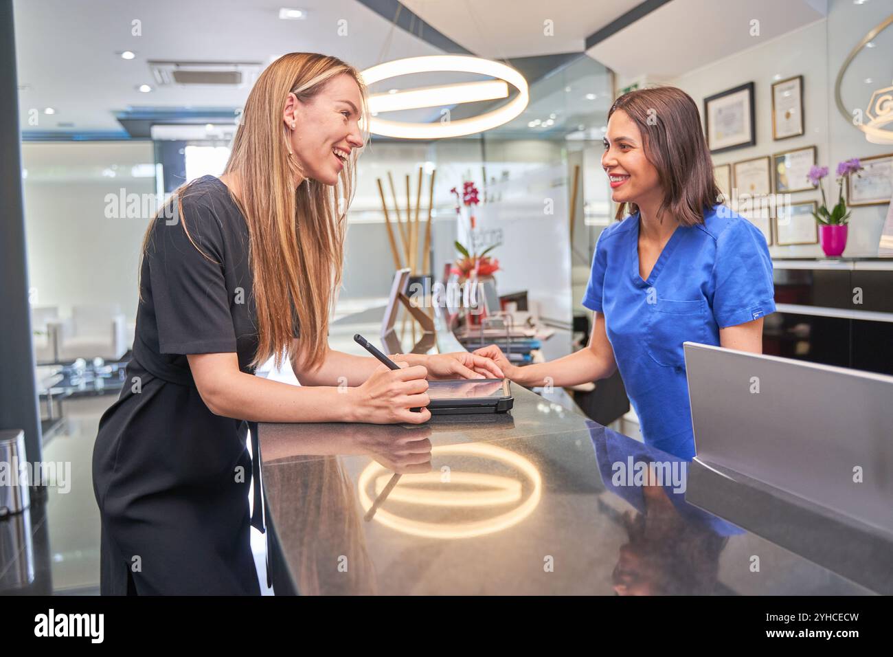 una donna al ricevimento di un dentista si riempie i suoi dettagli per una procedura dentale, si guardano l'un l'altro e sorridono Foto Stock