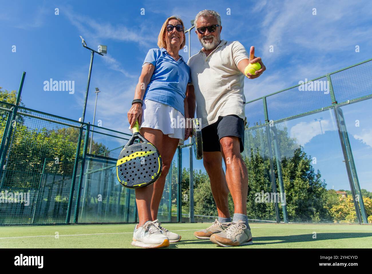vista a basso angolo di due giocatori anziani che celebrano la loro vittoria sul campo. Sorridono e sollevano i pollici verso la fotocamera, espr Foto Stock