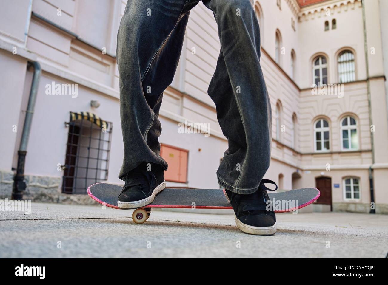 Skateboarder che fa il trick in Urban Street. Primo piano dello skater che indossa jeans larghi in equilibrio sullo skateboard. Concetto di sottocultura giovanile Foto Stock
