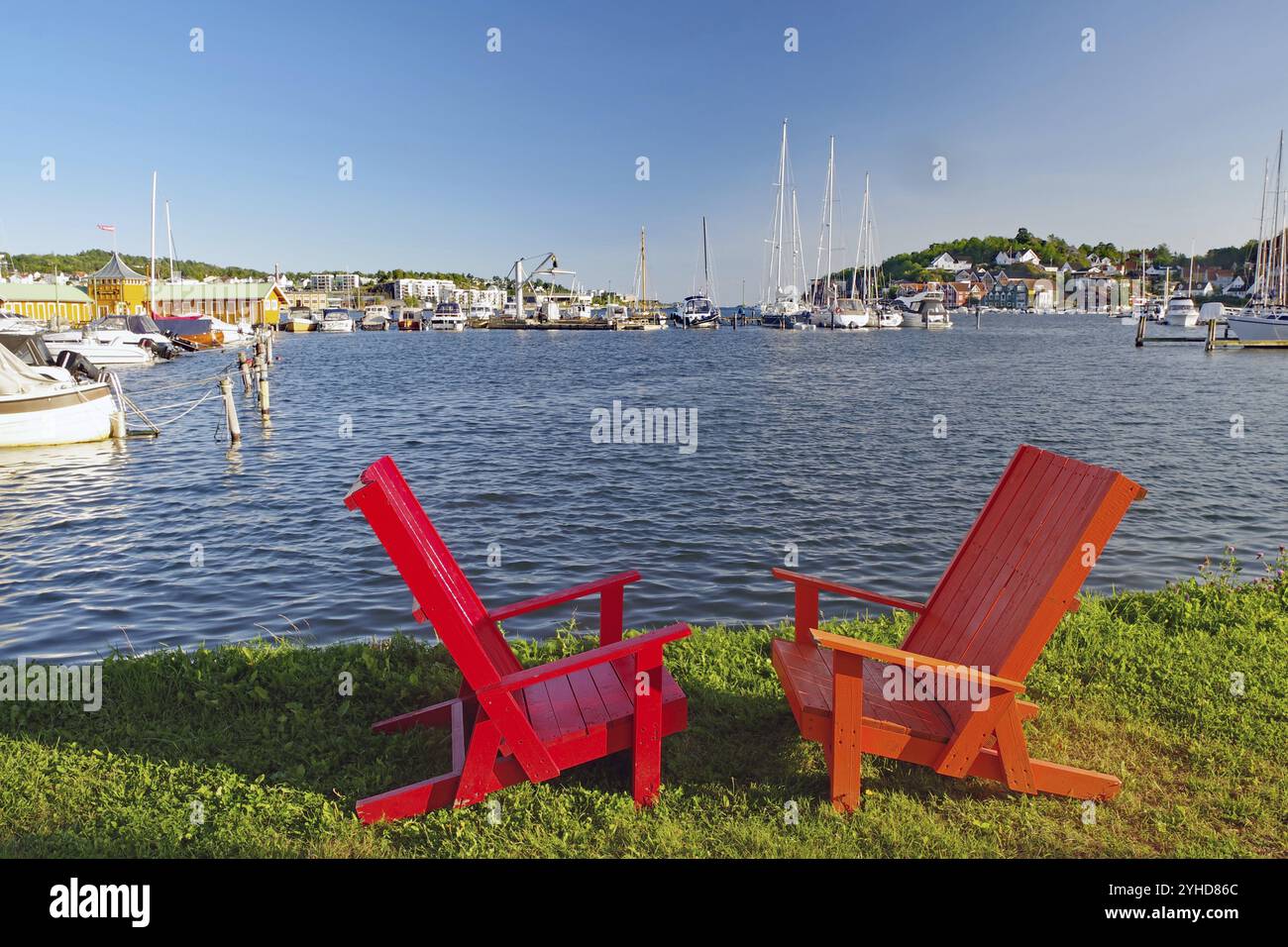 Due sedie di legno rosse su un prato che si affaccia su un porto soleggiato, Sandefjord, Norvegia, Europa Foto Stock