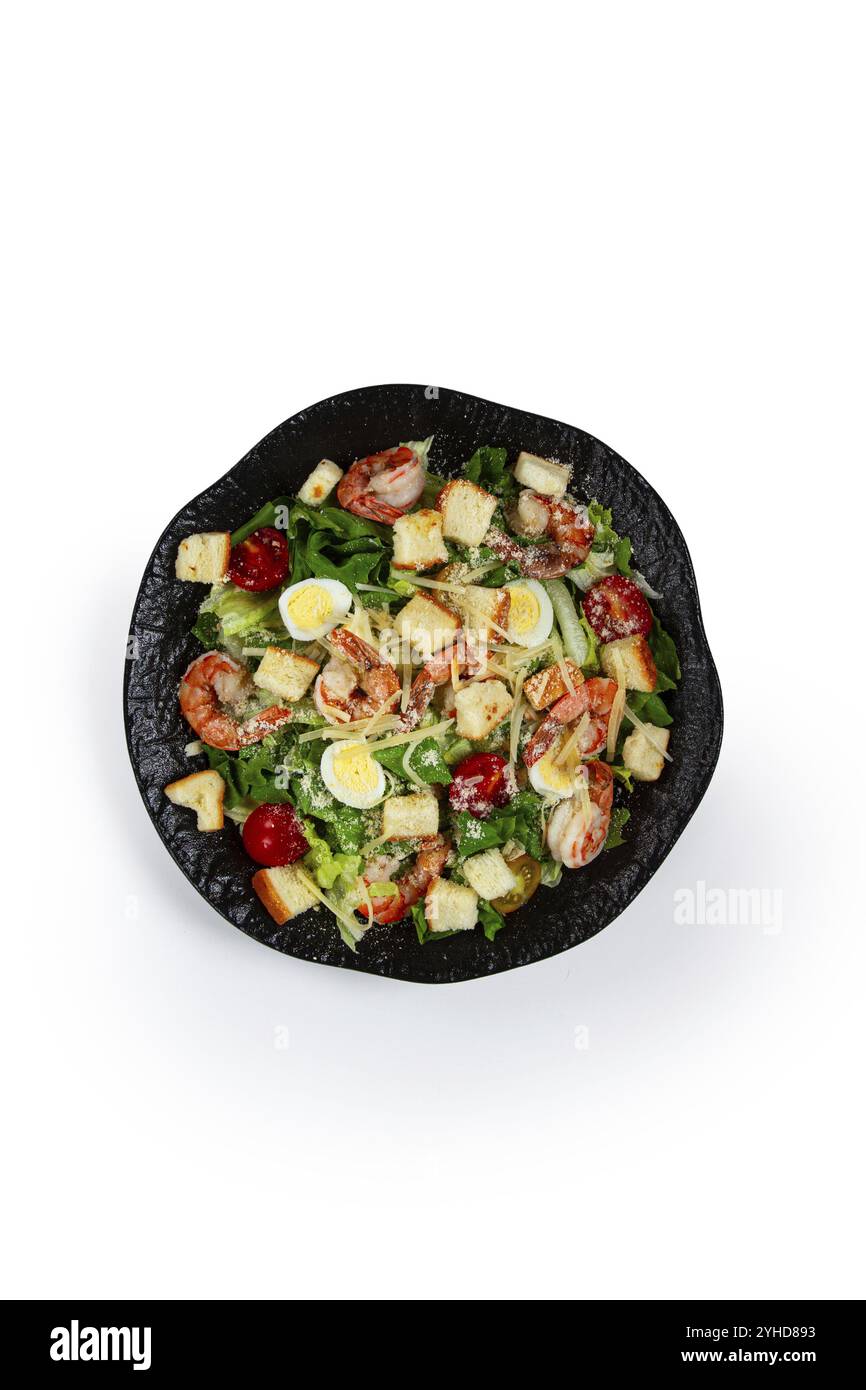 Caesar Salad con gamberi tigre, insalata di gamberi, foglie di lattuga, uova di quaglia, pomodori ciliegini, parmigiano, su un piatto nero, isolare Foto Stock