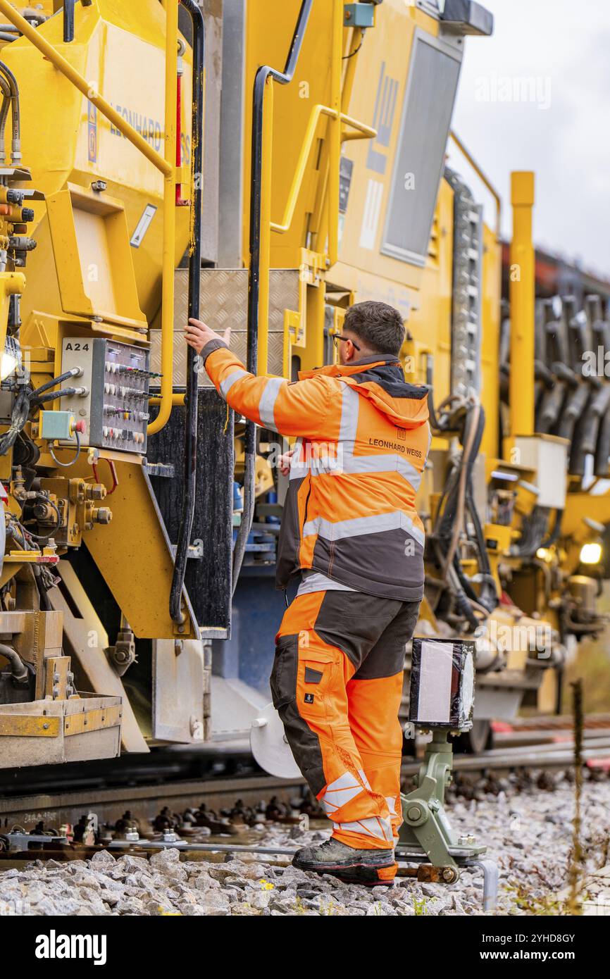 Un lavoratore interagisce con grandi macchine gialle su una linea ferroviaria, costruzione di binari Hermann Hesse Bahn, distretto di Calw, Foresta Nera, Germania, Europ Foto Stock