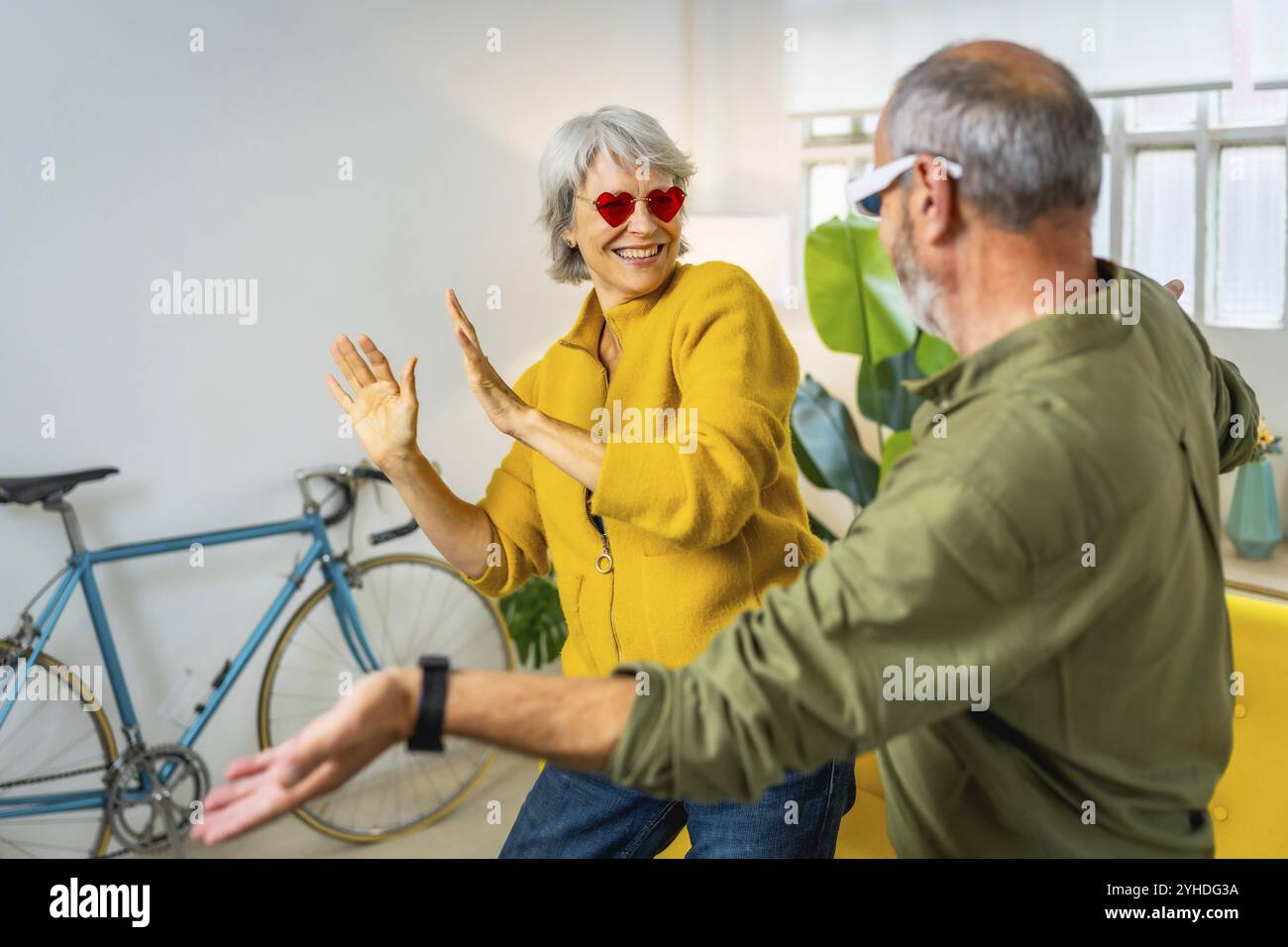 Moderna coppia senior con eleganti occhiali da sole che si divertono insieme a casa ridendo e ballando Foto Stock