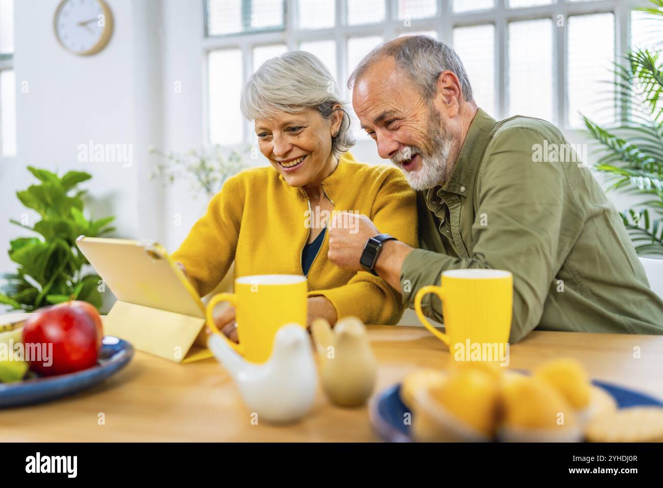 Felice coppia di anziani sposata che usa un tablet insieme mentre condivide la colazione a casa Foto Stock
