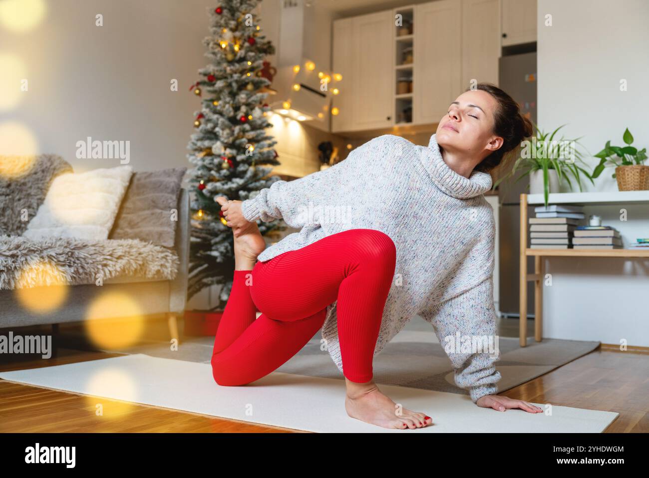 Donna che fa yoga a casa in salotto contro l'albero di Natale. Esercizio di stretching. Tempo per me durante Natale. Foto Stock