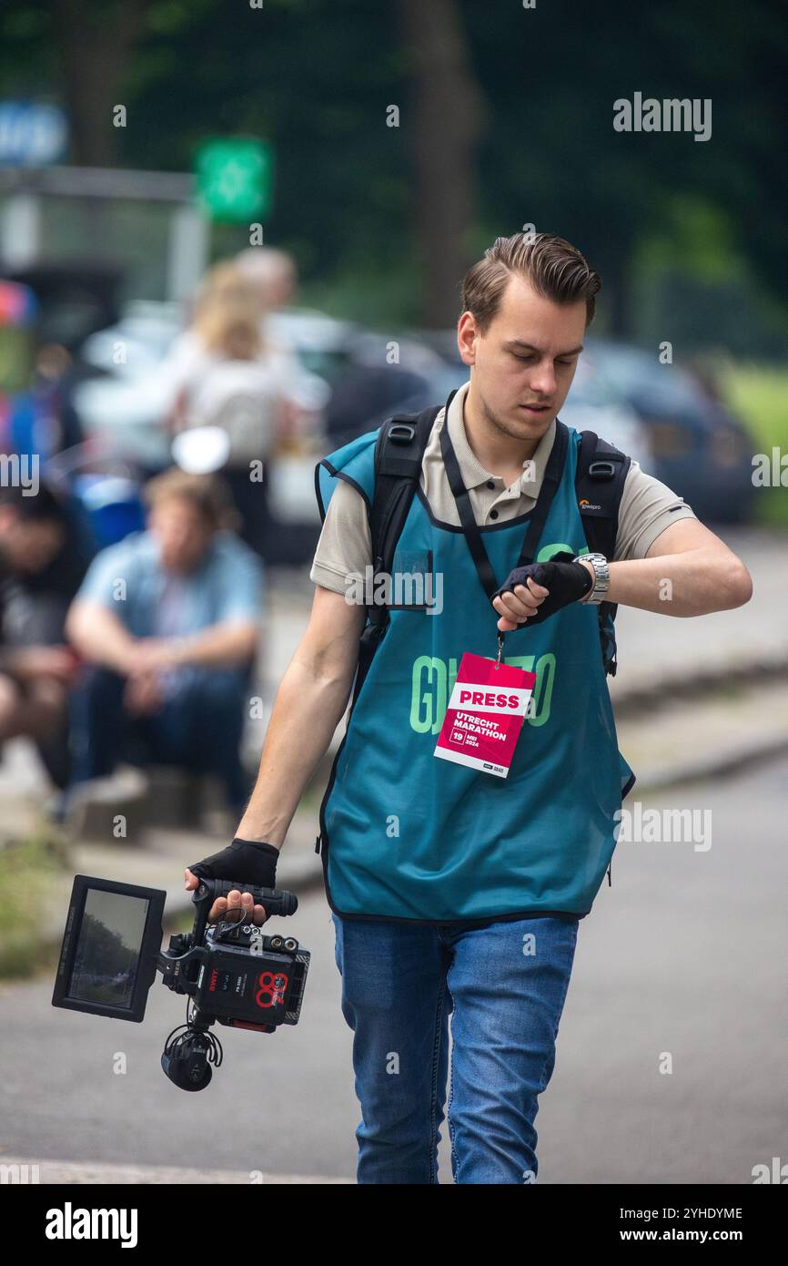 Utrecht, regione di Utrecht, Paesi Bassi - 19.05.2024: Un giovane fotografo di stampa che indossa un giubbotto di tè e un distintivo rosso "Press" cammina mentre controlla il suo wri Foto Stock