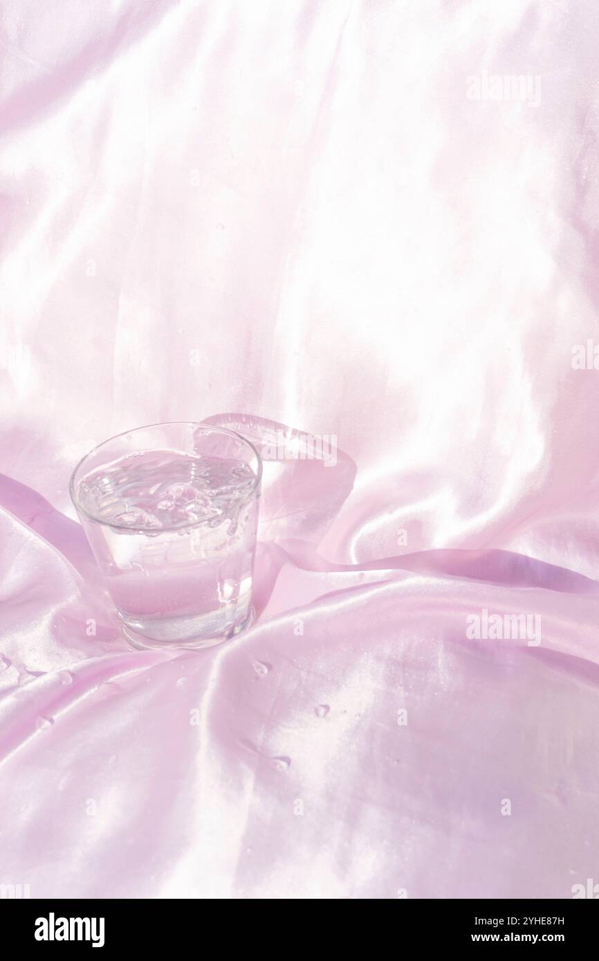 Rinfrescante bicchiere d'acqua su tessuto di seta rosa Foto Stock