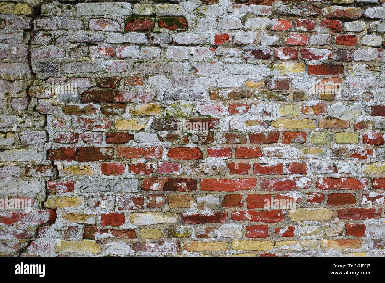 Mura rustiche molto vecchie con mattoni gialli e rossi. C'è una crepa nel muro. I resti di vernice bianca sono visibili Foto Stock