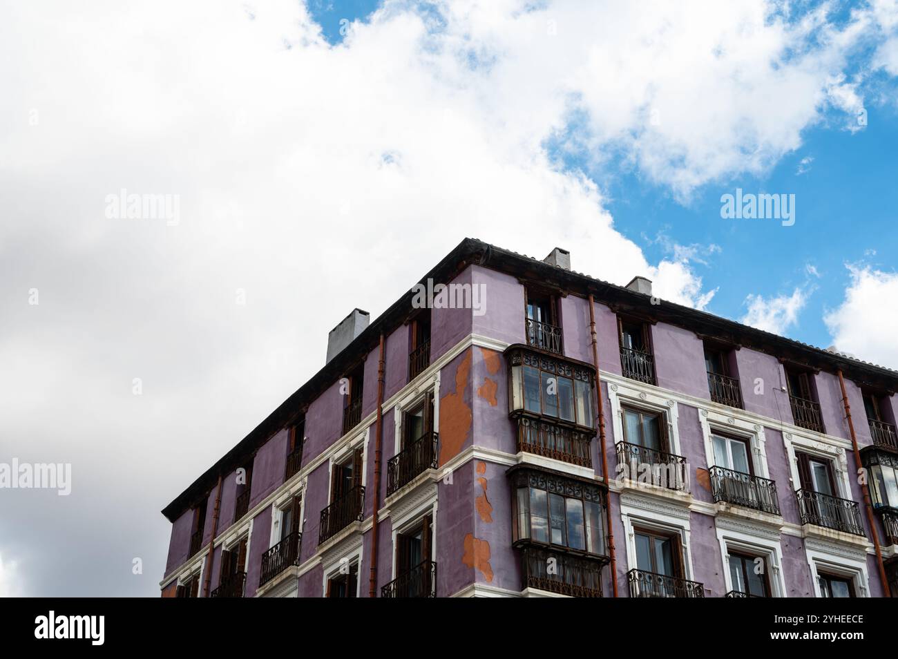 L'angolo di un edificio viola intemprato con balconi a Madrid, incorniciato contro un cielo nuvoloso, mostra il fascino senza tempo e la bellezza rustica Foto Stock