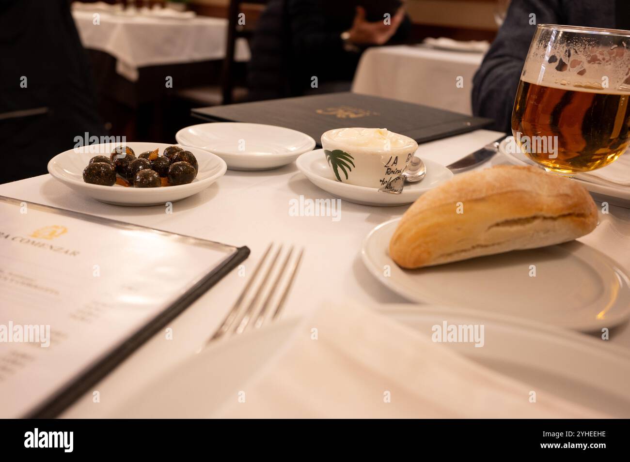 Un piatto di olive nere condite, abbinato a una pagnotta di pane fresco e crema burro all'aglio, offre un'autentica esperienza culinaria mediterranea Foto Stock