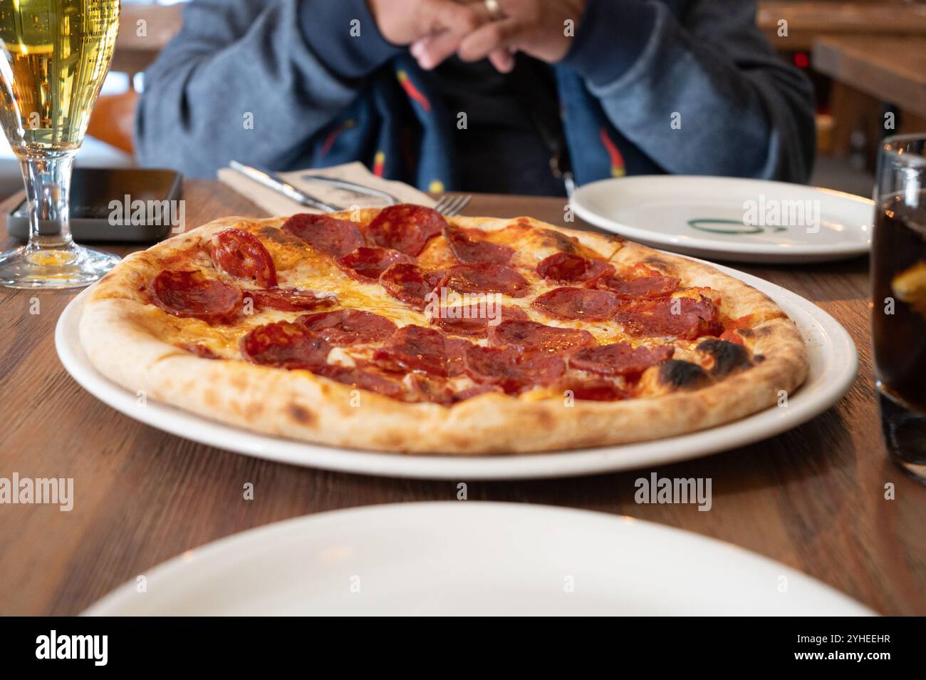 Un pranzo informale ma gustoso in un ristorante accogliente, caratterizzato da una grande pizza non tagliata, gustata da una coppia in un ambiente intimo Foto Stock