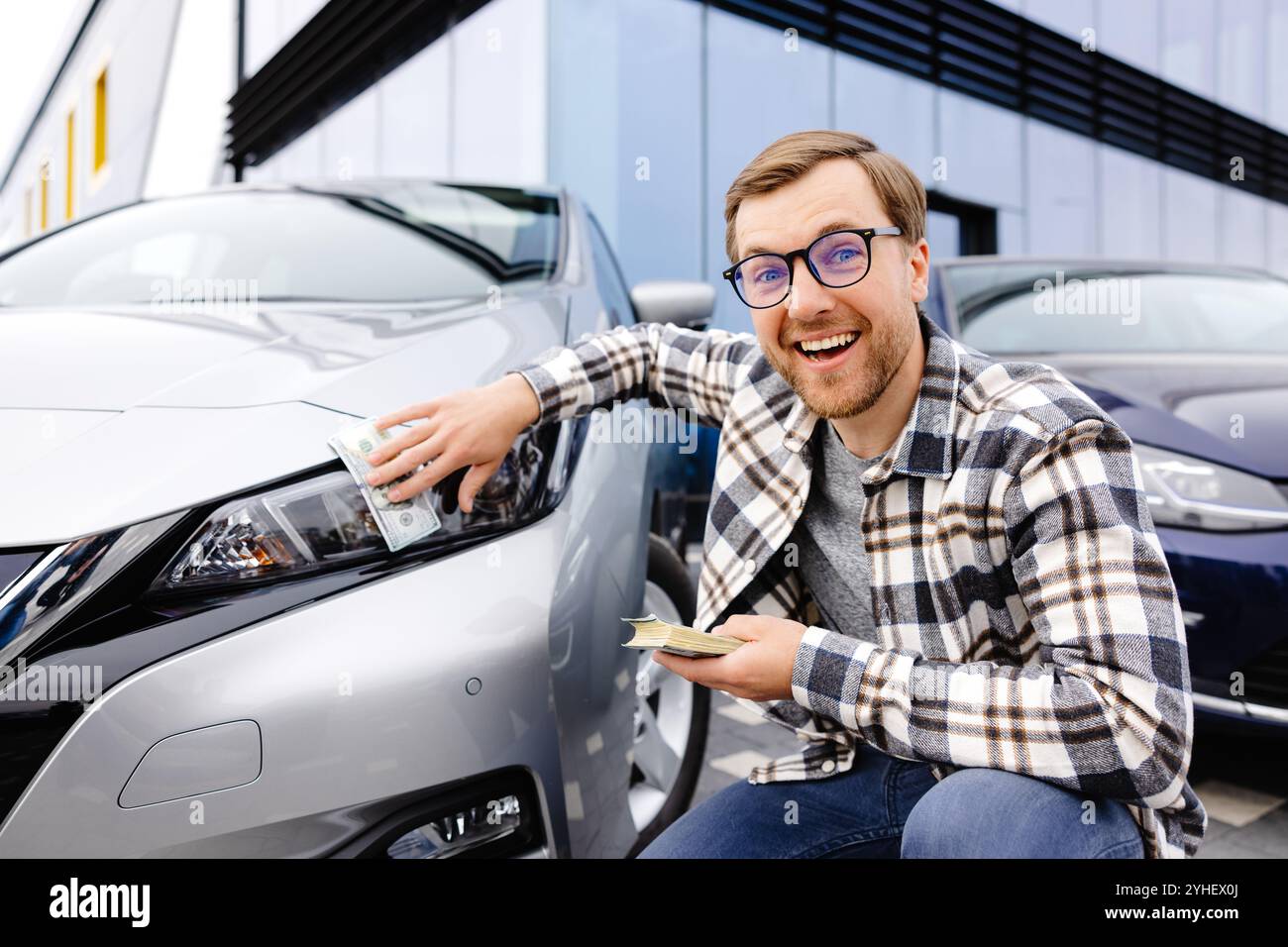 Giovane uomo che tiene i soldi in mano in piedi auto anteriore e preparare paga a rate - assicurazione, prestito e l'acquisto di auto concetto di assicurazione. Acquista e scendi pa Foto Stock