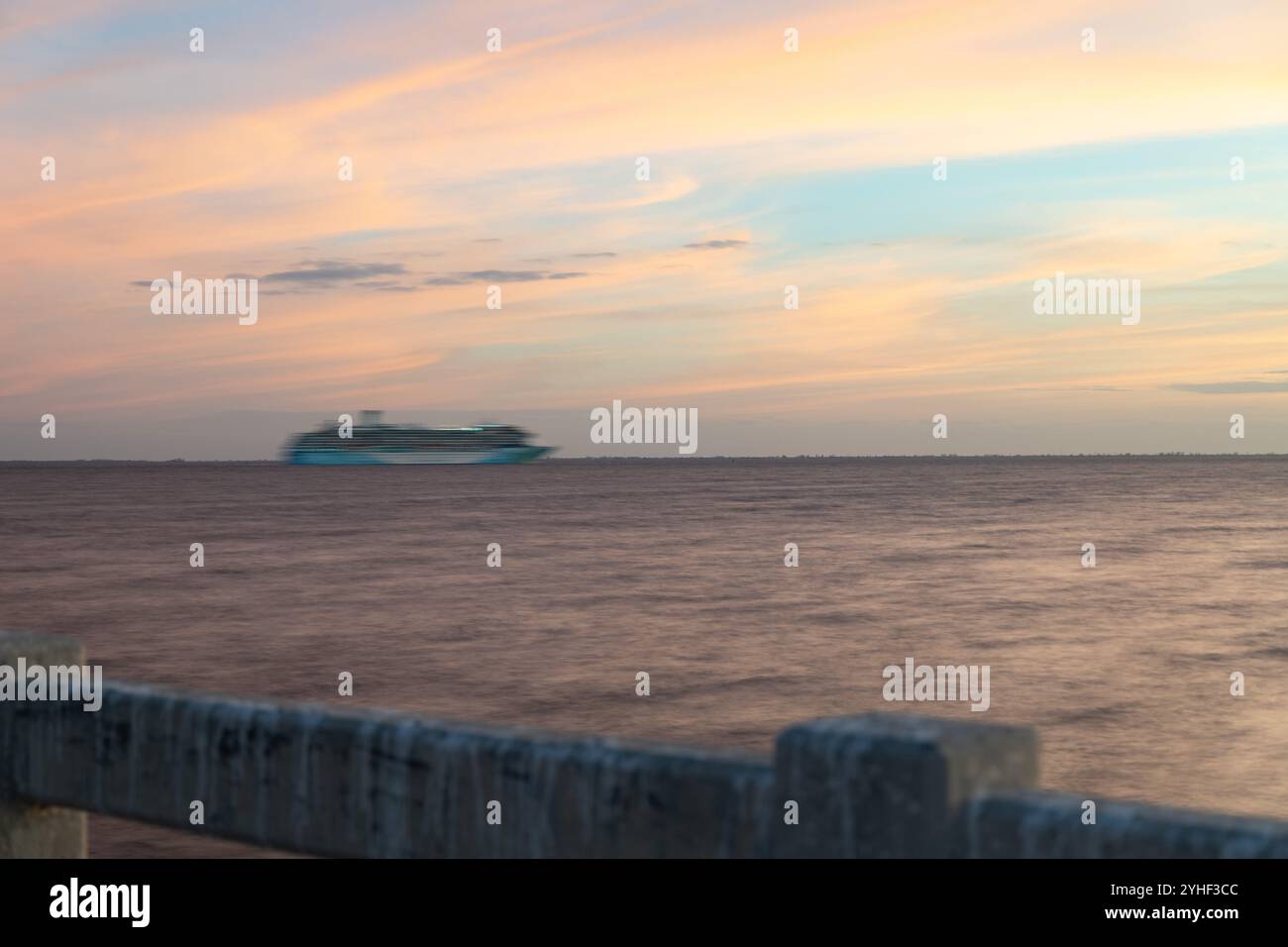 Un tramonto sereno proietta calde sfumature sulla Baia di Tampa, creando un'atmosfera tranquilla. Un movimento sfocato in lontananza da una nave che passa, aggiungendo un elemento dinamico Foto Stock