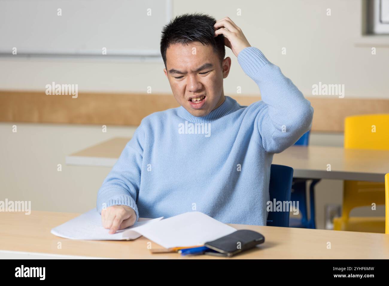 Un giovane studente universitario è confuso e si gratta la testa perché non sa come risolvere un problema difficile nel suo test Foto Stock