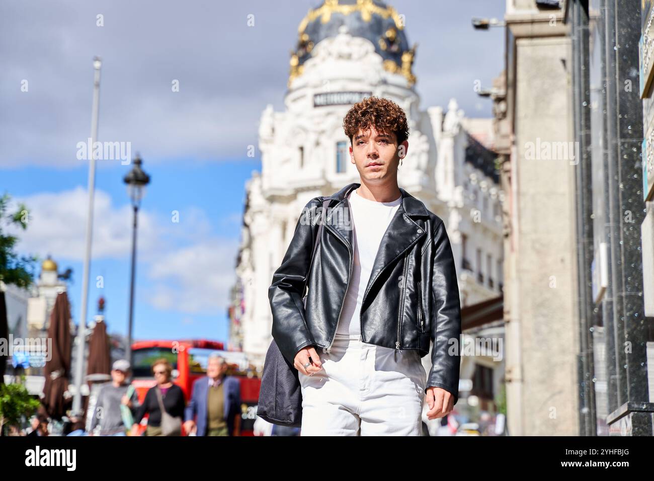 Un giovane uomo che indossa una giacca di pelle cammina per strada con una borsa Foto Stock