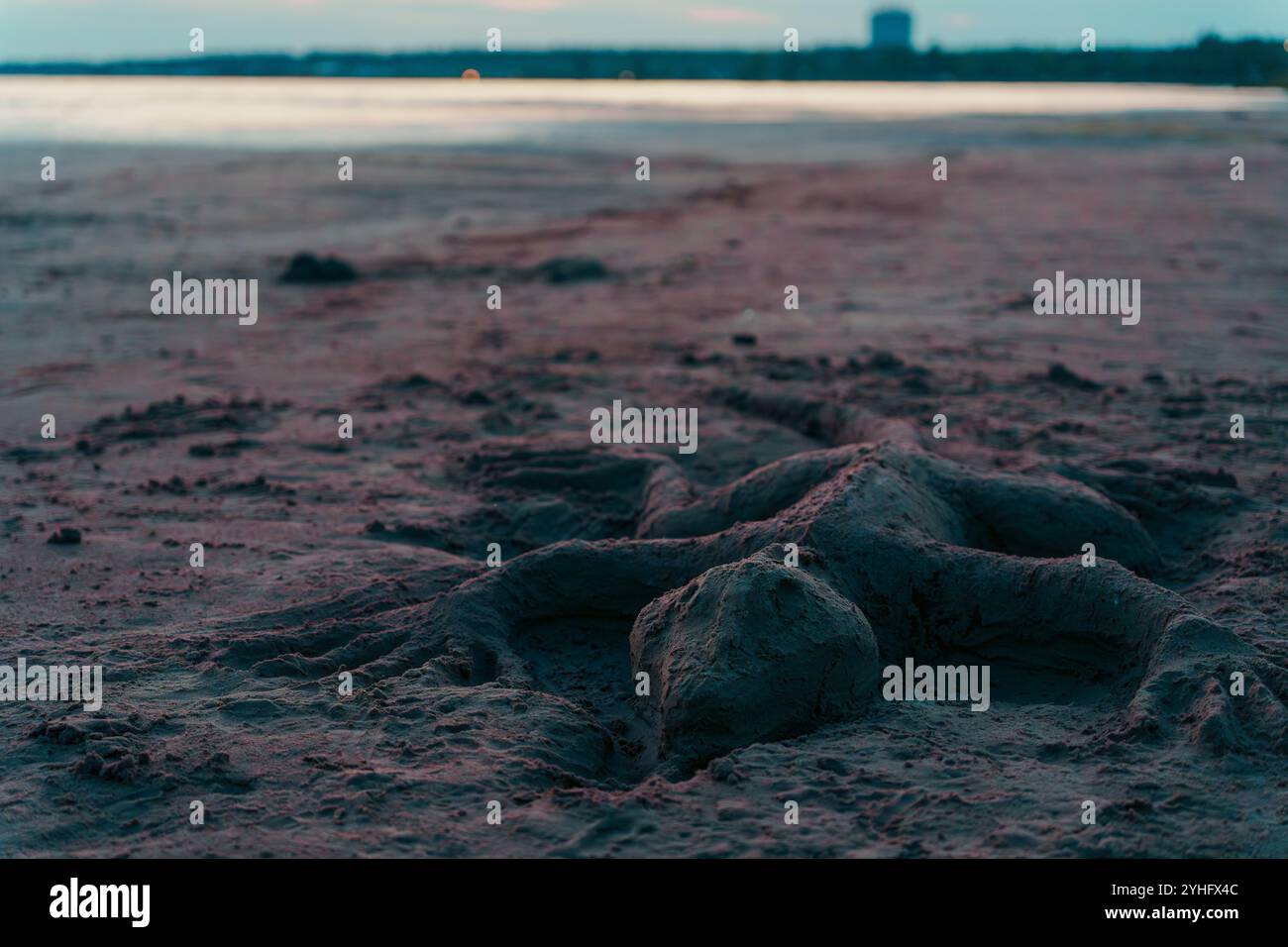 Una scultura di sabbia a forma di lucertola si appoggia su una spiaggia al crepuscolo, con una leggera luce serale che proietta ombre morbide, catturando una scena serena e creativa da parte del Foto Stock