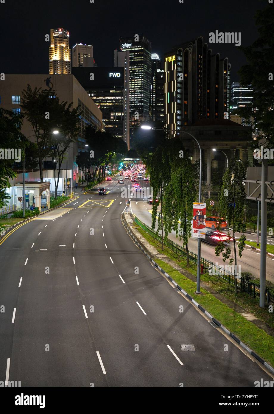 Una strada vuota di notte che conduce alla città di Singapore con grattacieli in lontananza. Foto Stock