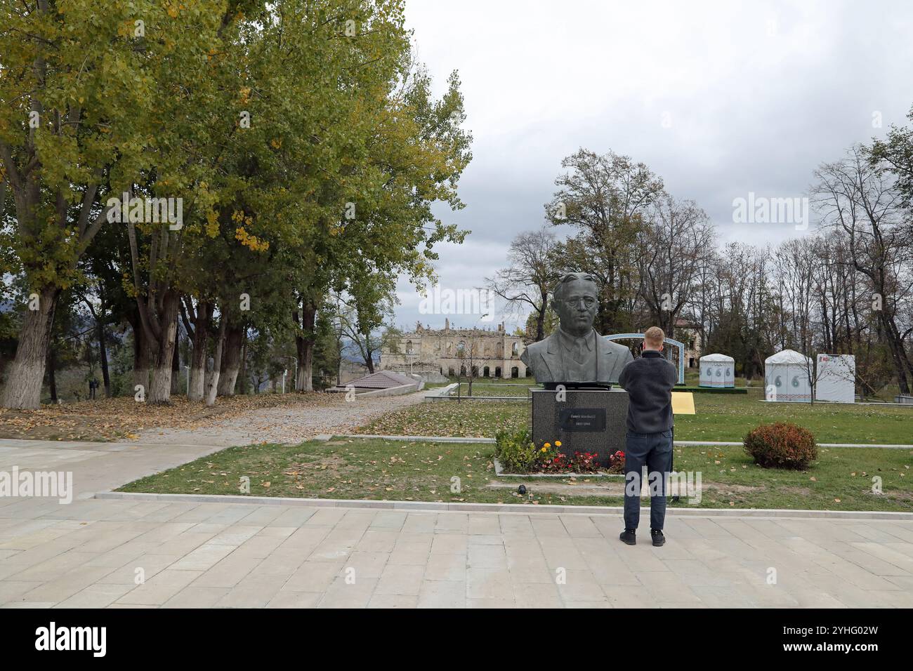 Turista che scatta una foto del proiettile danneggiato busto di Hajibekov in epoca sovietica a Shusha Foto Stock