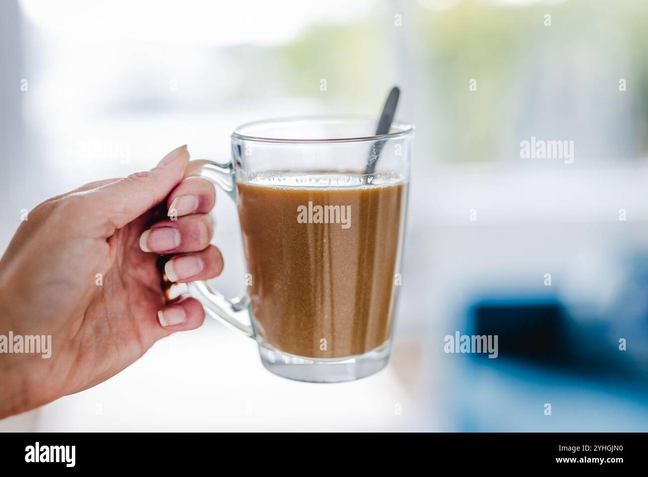 mano che tiene il caffè in una tazza trasparente davanti allo sfondo sfocato degli interni della casa, profondità di campo ridotta, abitudini e concetto di stile di vita Foto Stock mano che tiene il caffè in una tazza trasparente davanti allo sfondo sfocato degli interni della casa, profondità di campo ridotta, abitudini e concetto di stile di vita Foto Stock