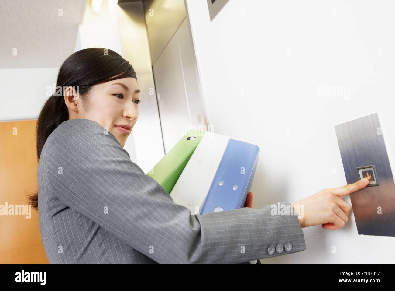 Donna in tuta che preme il pulsante dell'ascensore con molti documenti Foto Stock