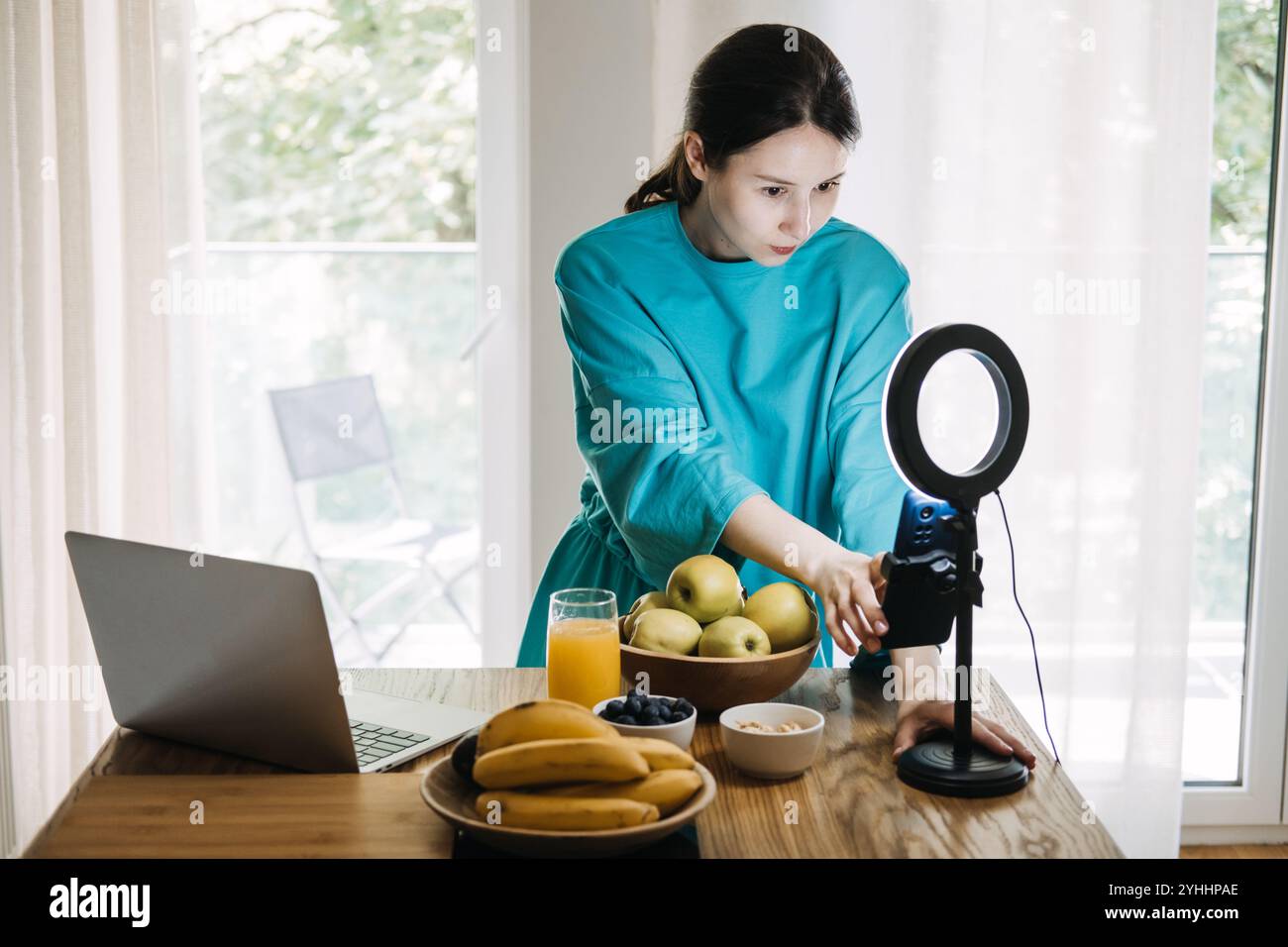 Giovane donna che filma contenuto di stile di vita sano con frutta e succo in cucina. Blog di benessere e concetto di influencer marketing Foto Stock