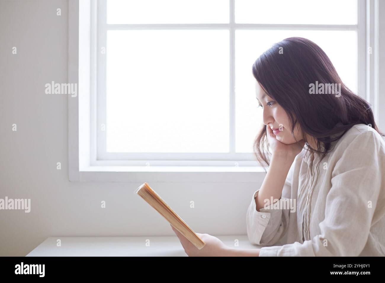 Giovane donna che legge un libro sui gomiti di profilo Foto Stock