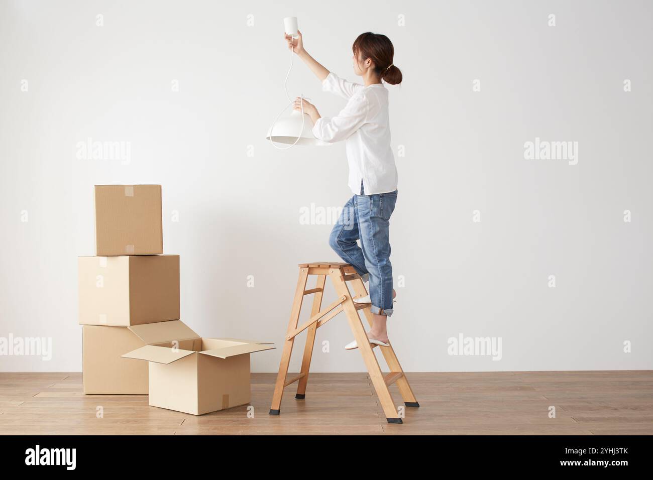 Pile di scatole di cartone e donna che attacca la lampada a sospensione Foto Stock