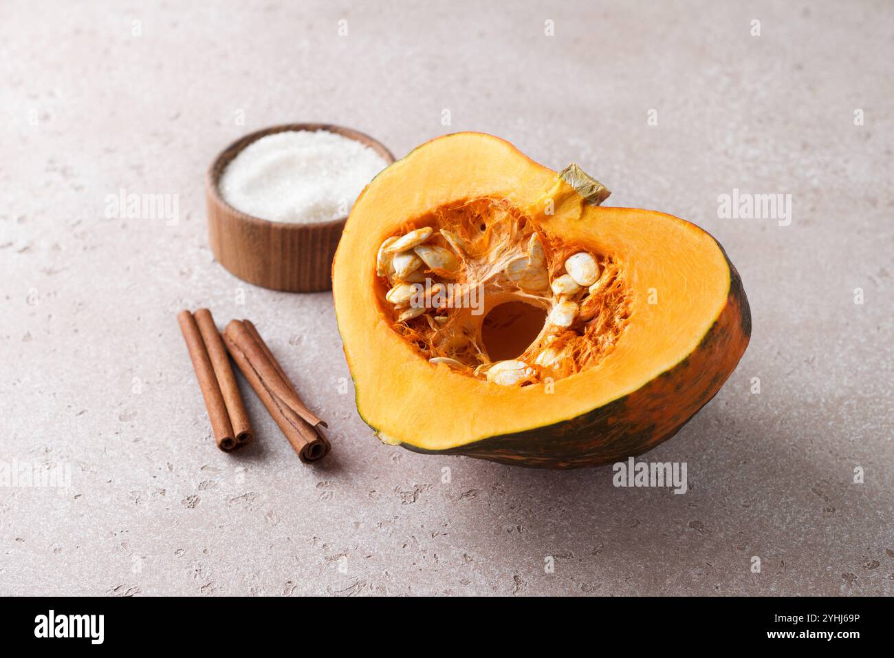 Tagliare la zucca cruda all'arancia con semi, cannella e zucchero su uno sfondo beige a pietra. Preparazione della zucca per la cottura. Foto Stock