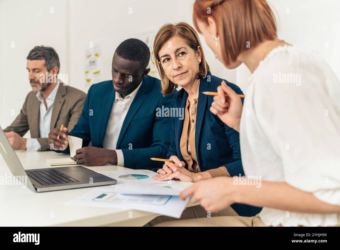 Dirigente donna maturo che guida team aziendali diversificati durante l'incontro di analisi finanziaria con professionisti multigenerazionali che esaminano i rapporti sui dati Foto Stock