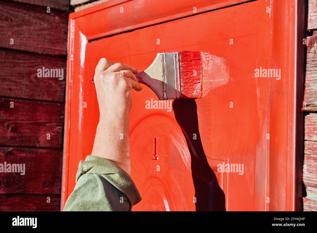 Tinteggiatura della porta d'ingresso in metallo della casa di campagna rossa con una spazzola piatta larga 100 mm. Foto Stock