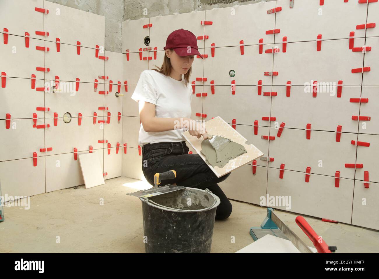 Donna che affianca le pareti del bagno, applica l'adesivo su una piastrella e posiziona la piastrella in ceramica nella giusta posizione. Processo di installazione delle piastrelle nel bagno Foto Stock