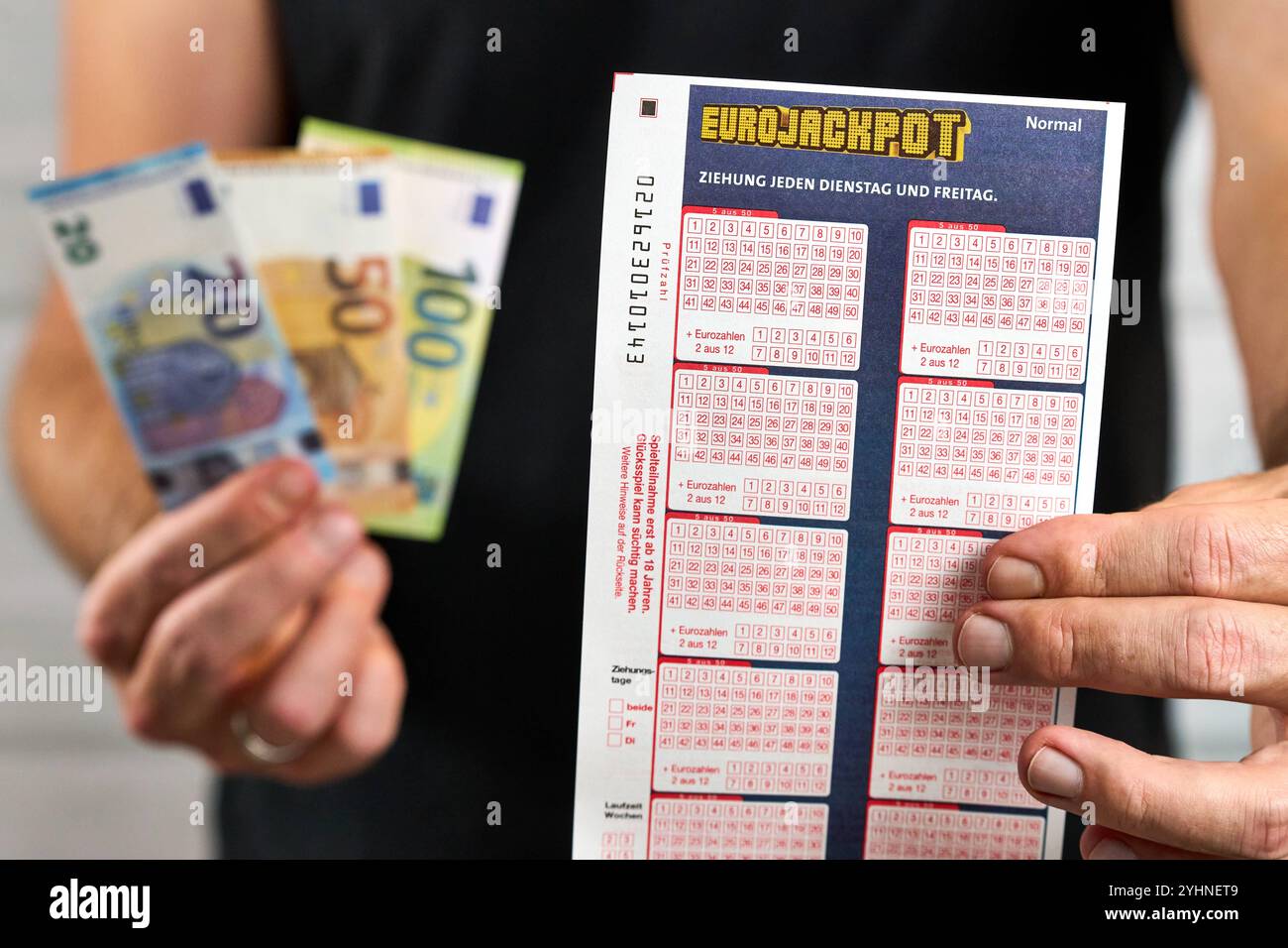 Baviera, Germania - 12 novembre 2024: Biglietto Eurojackpot o biglietto della lotteria. Symbol, il vincitore ha in mano il biglietto fortunato, accanto alle banconote e alle vincite in euro del gioco d'azzardo. *** Eurojackpot Tippschein, bzw. Spielschein der Lotterie. Symbol, Gewinner hält Glückslos in der Hand, neben Geldscheinen und Euro-Gewinn des Glücksspieles. Foto Stock