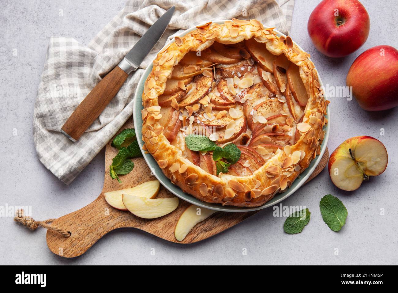 galette di mele appena sfornata decorata con scaglie di mandorle e menta, servita su un tavolo con mele fresche e un coltello Foto Stock