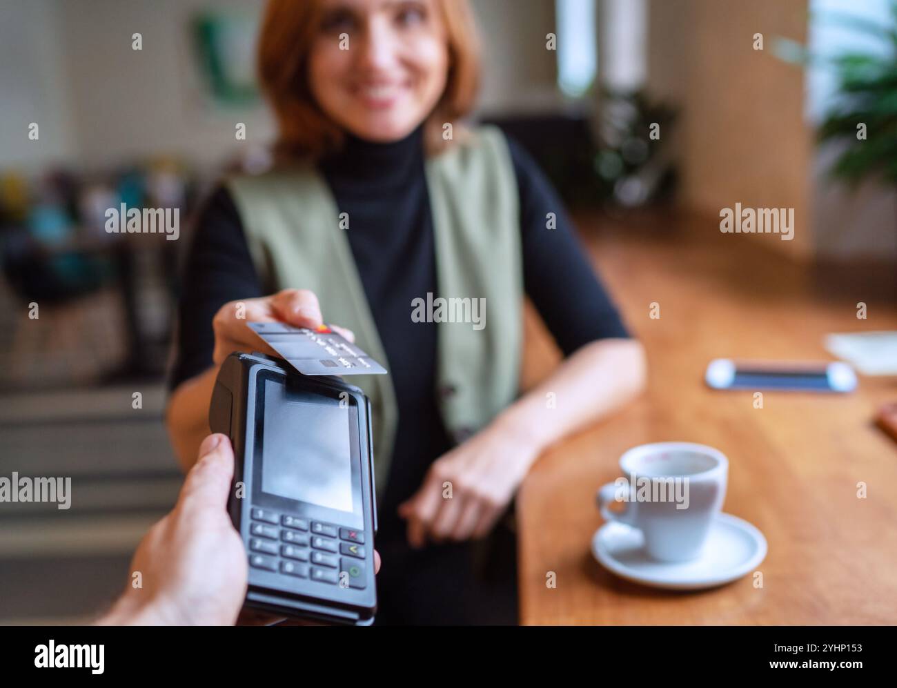 Una giovane donna che detiene un credito che effettua pagamenti bancari wireless con il processo del terminale POS acquisisce al tavolo del bar/caffetteria/ristorante al coperto. Concentrati sulla mach Foto Stock
