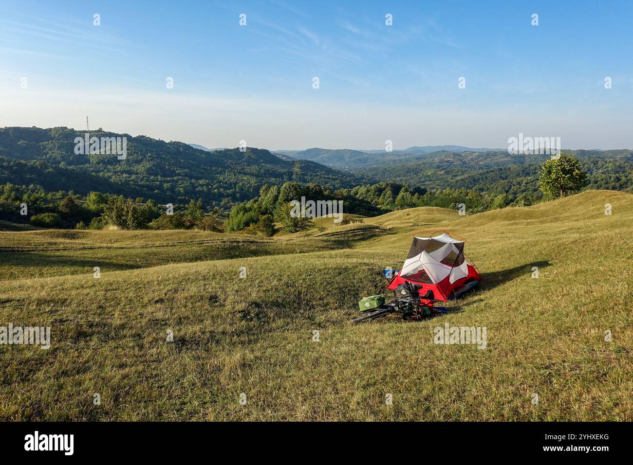 Tenda da da campeggio rossa e bianca MSR Hubba Hubba NX con bici da turismo allestita su una collina erbosa che si affaccia su una vasta distesa di colline ondulate in Romania Foto Stock