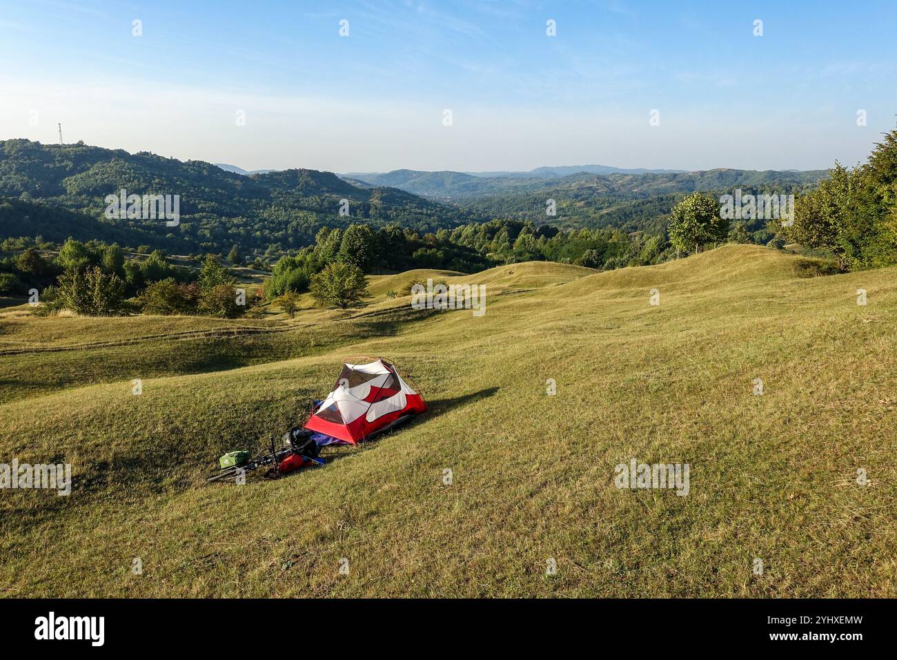 Tenda da da campeggio rossa e bianca MSR Hubba Hubba NX con bici da turismo allestita su una collina erbosa che si affaccia su una vasta distesa di colline ondulate in Romania Foto Stock