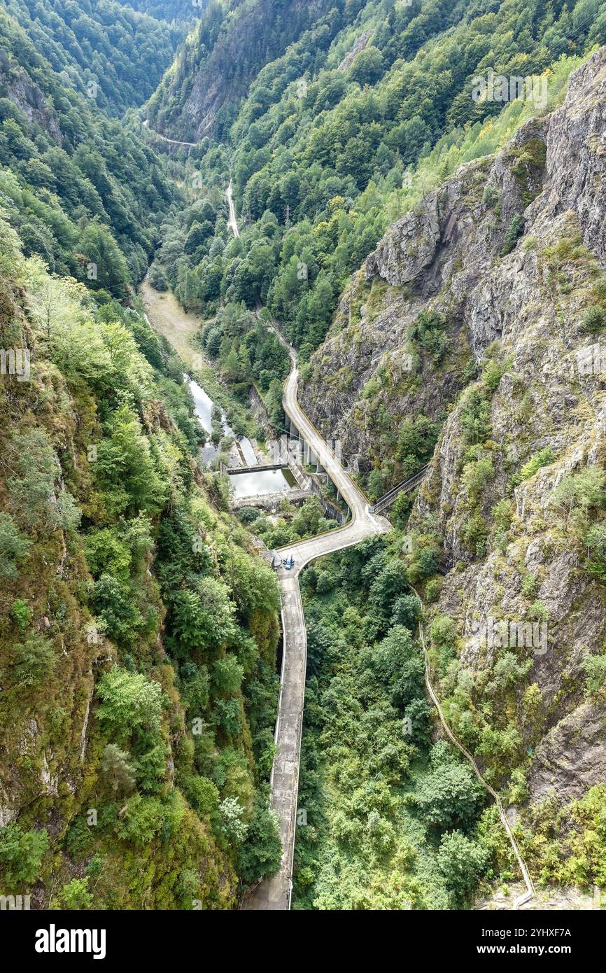 La diga di accesso tortuosa strada di montagna che attraversa una profonda gola boscosa con ripide scogliere rocciose su entrambi i lati, alla diga di Vidraru, Transfăgărășan Foto Stock