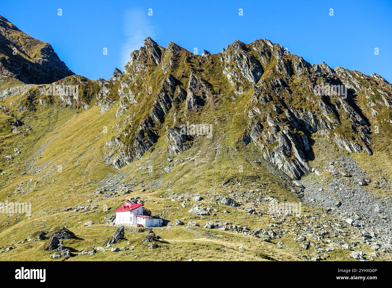 Rifugio di montagna a Balea, Transfăgărășan, Romania, con tetto rosso annidato alla base di aspre cime rocciose sotto un cielo azzurro Foto Stock