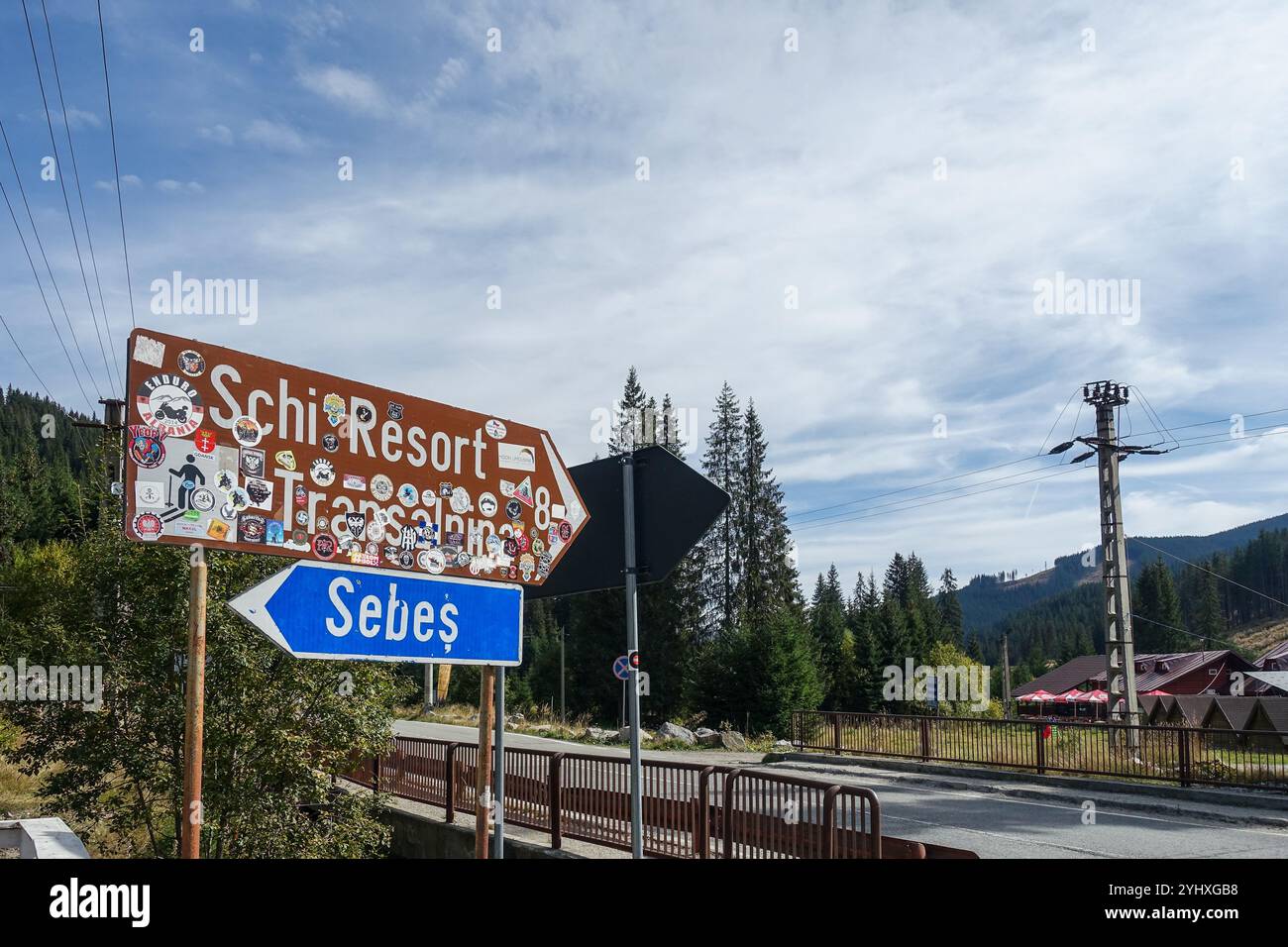 Cartelli stradali che indicano una stazione sciistica nella regione montuosa di Obârşia Lotrului, Romania, con un paesaggio forestale e un cielo limpido sullo sfondo Foto Stock