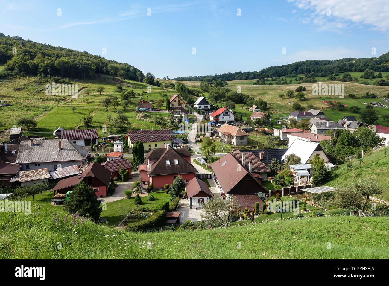 Vista panoramica del pittoresco villaggio di Banský Studenec immerso in verdi colline sotto un cielo azzurro, con case incantevoli e vegetazione lussureggiante Foto Stock
