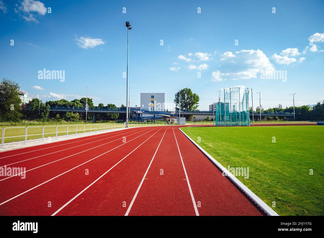 Vista di un moderno stadio di atletica con pista rossa a 8 corsie, immerso in vivaci campi verdi e circondato da un tranquillo paesaggio naturale Foto Stock