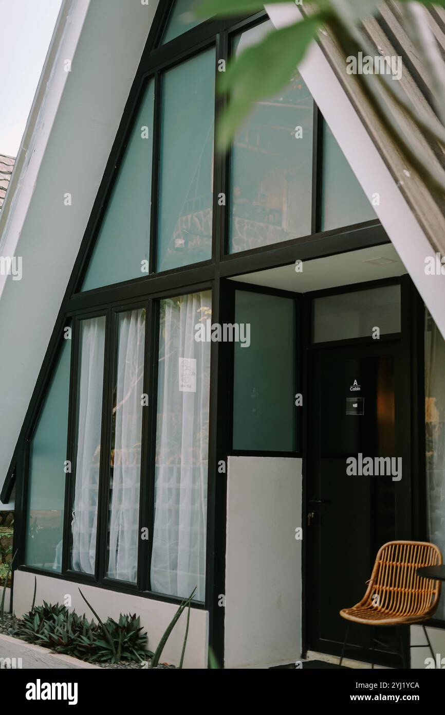 Cabina moderna con telaio Ad A con grandi finestre e un'estetica minimalista. Una sedia in vimini si siede all'esterno, esaltando la sua atmosfera accogliente ed elegante e si fonde con na Foto Stock