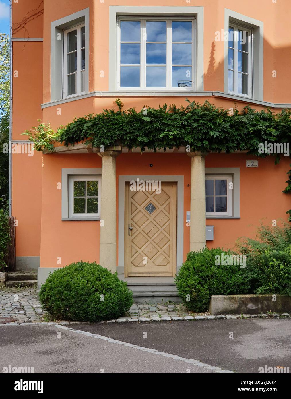 Casa arancione in una piccola città. Edificio compatto con porta d'ingresso al primo piano e balcone vetrato. Foto Stock